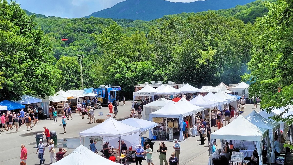 Tons of white tents set up in parking lot for art festival, trees and mountains in background