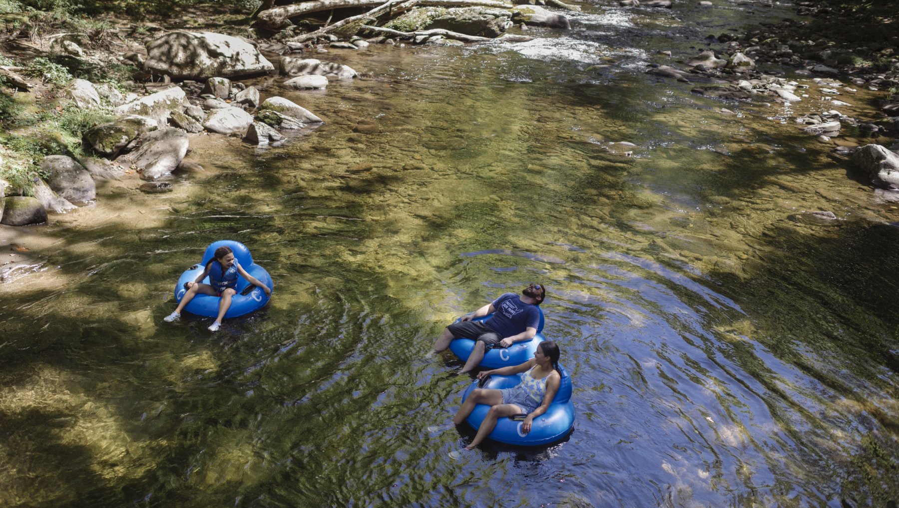 Aerial of father and two kids tubing down river in NC mountains.
