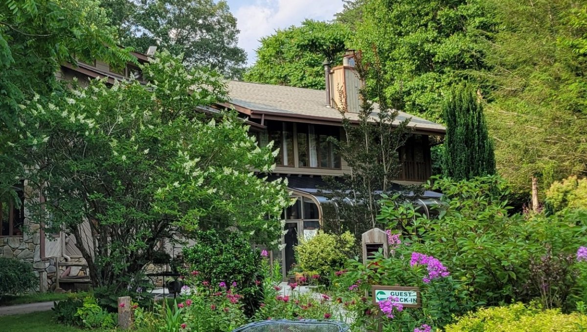 The outline of an Inn peaks out from behind blooming trees and flowers underneath a bright blue sky. 