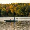 Father and son in fishing boat on lake with fall foliage in background.