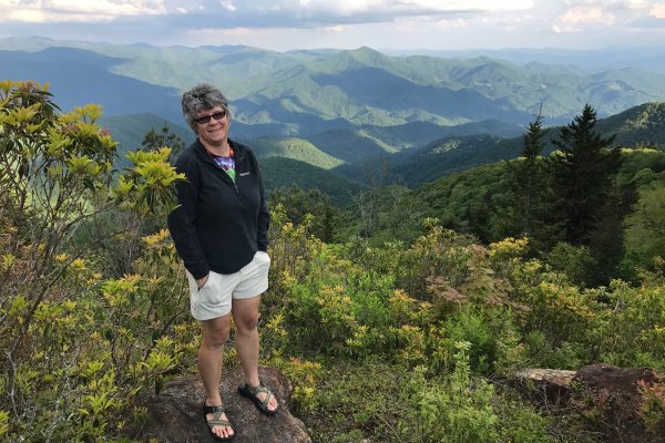 Woman standing on rock smiling at camera with beautiful mountains in background